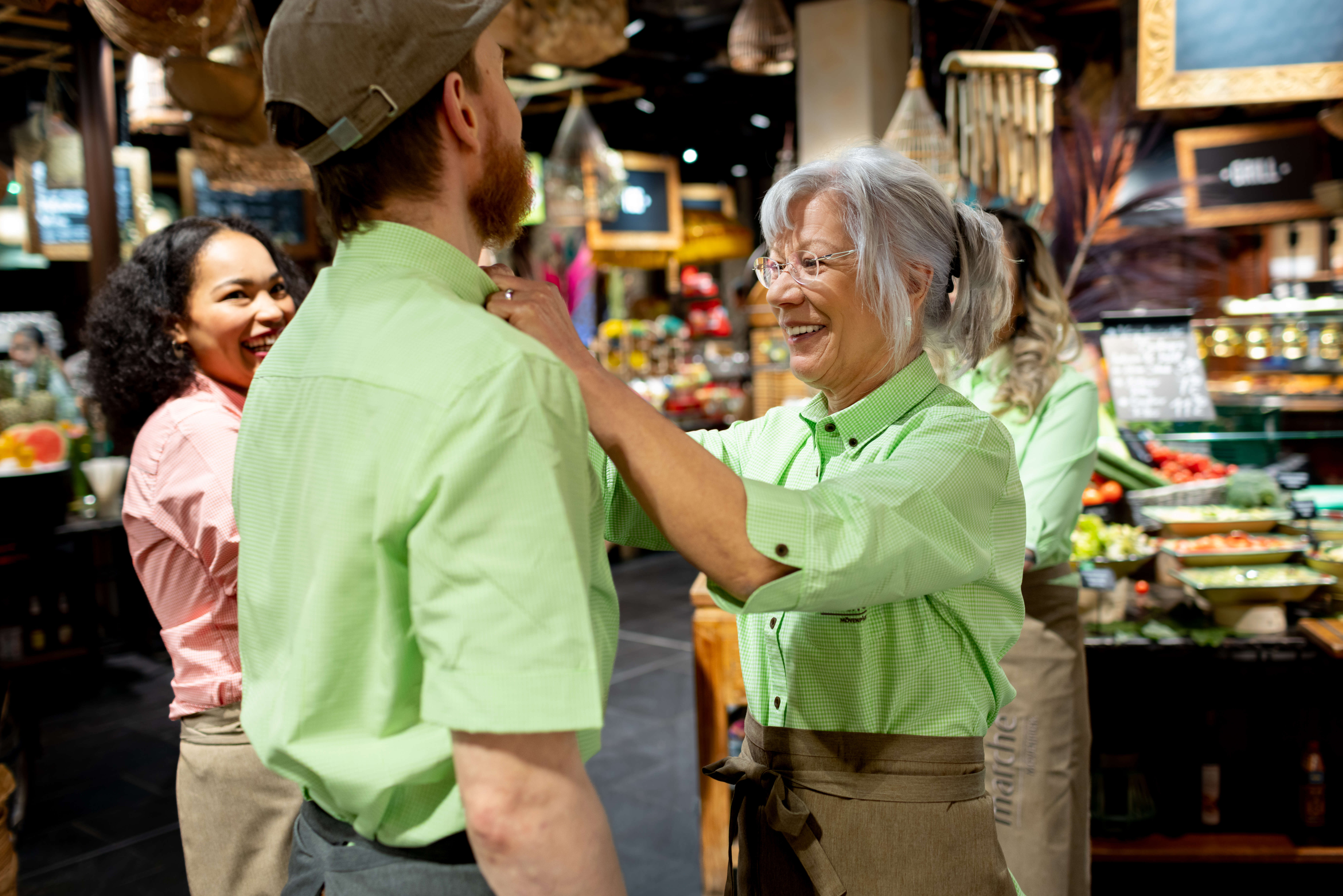 erfahrene Servicefrau hilft Azubi mit der Schürze