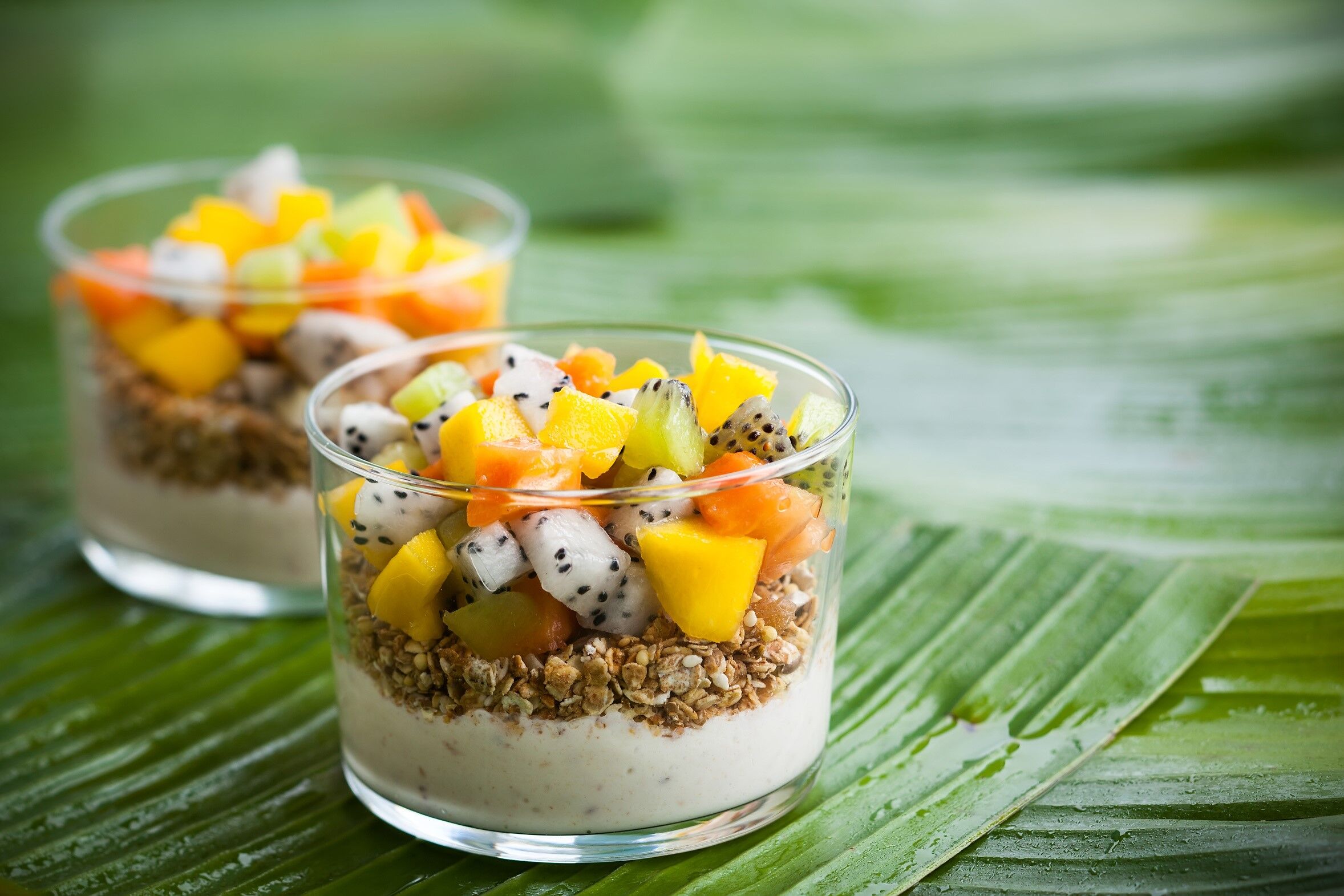 tropisches Müsli mit Früchten in einem Glas auf einem Bananenblatt