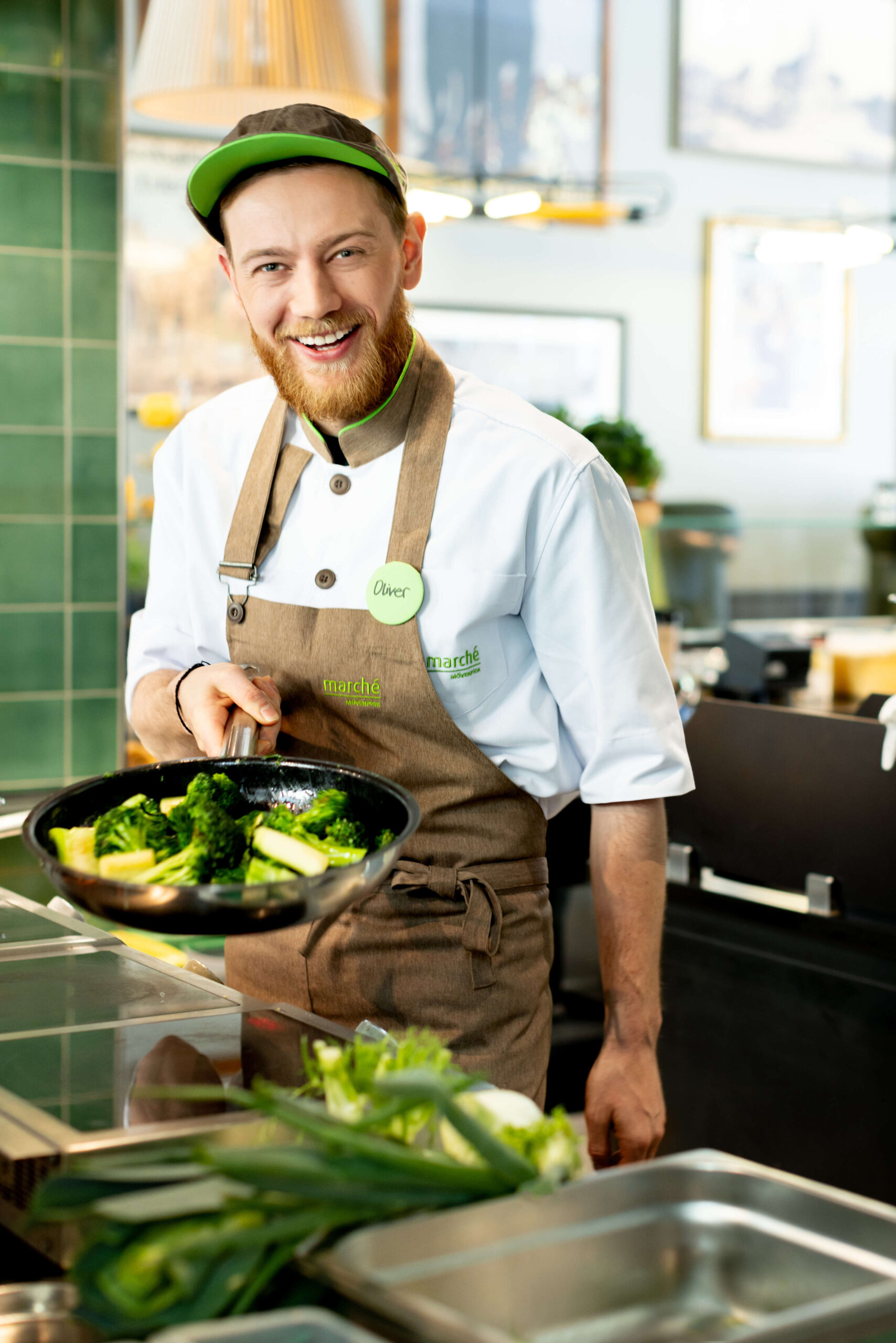 lachender Koch mit einer Pfanner voller grünem Gemüse