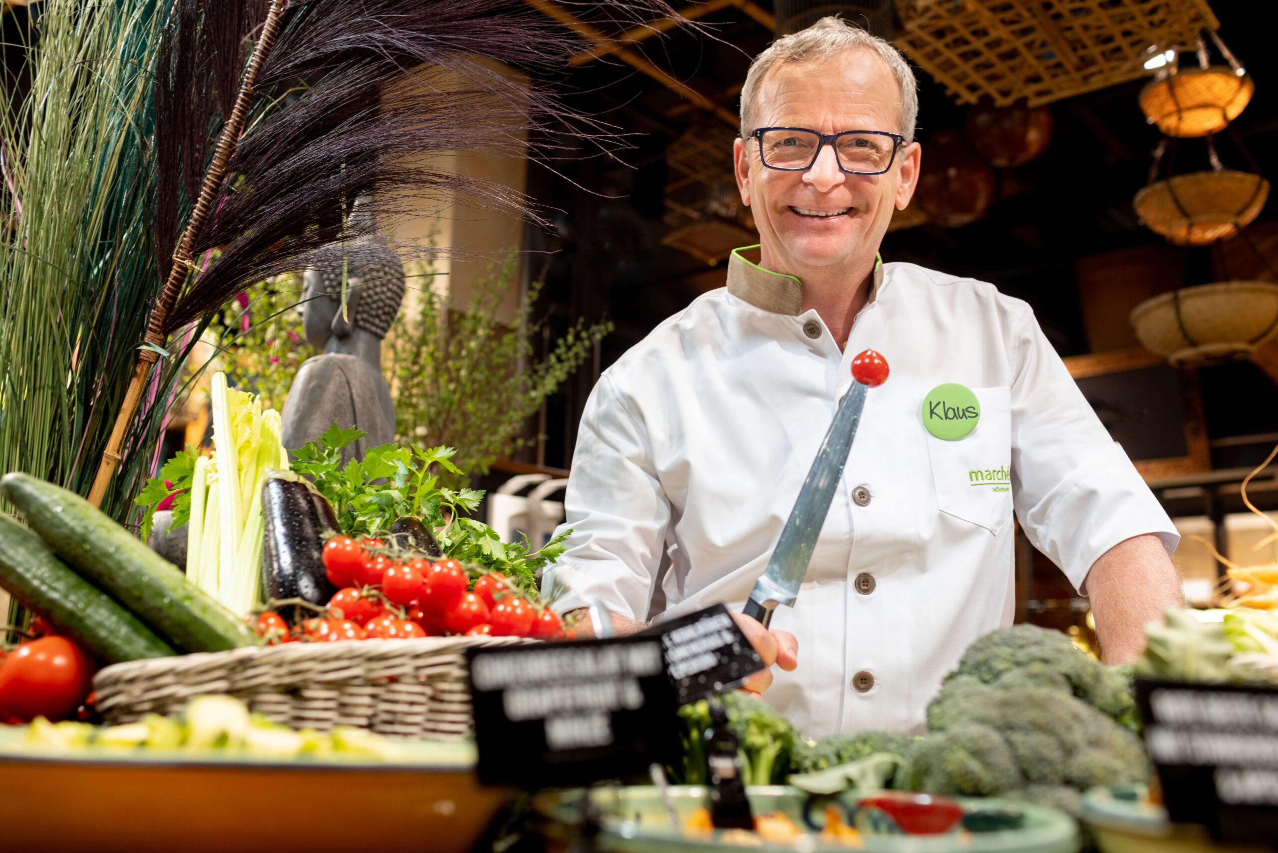 lachender Koch mit einem Messer, auf dem eine Tomate steckt